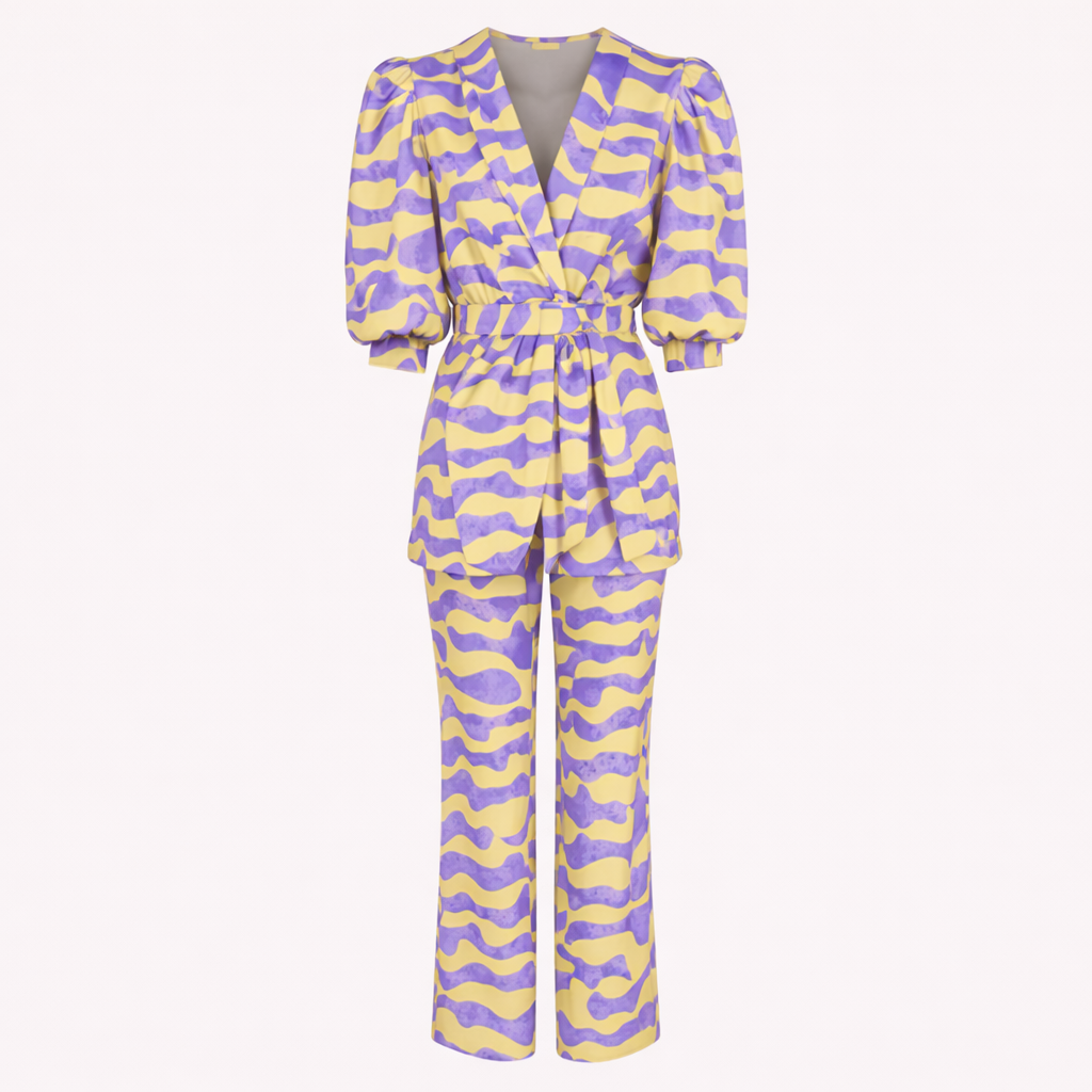 Una mujer posando al aire libre con un conjunto estampado de dos piezas, compuesto por blazer y pantalón, y un bolso de mano.