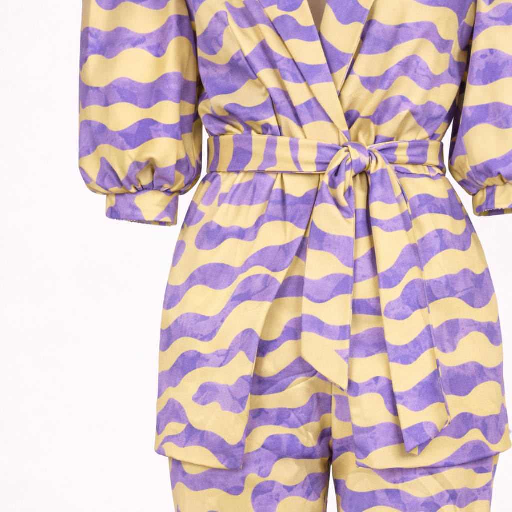 Una mujer posando al aire libre con un conjunto estampado de dos piezas, compuesto por blazer y pantalón, y un bolso de mano.